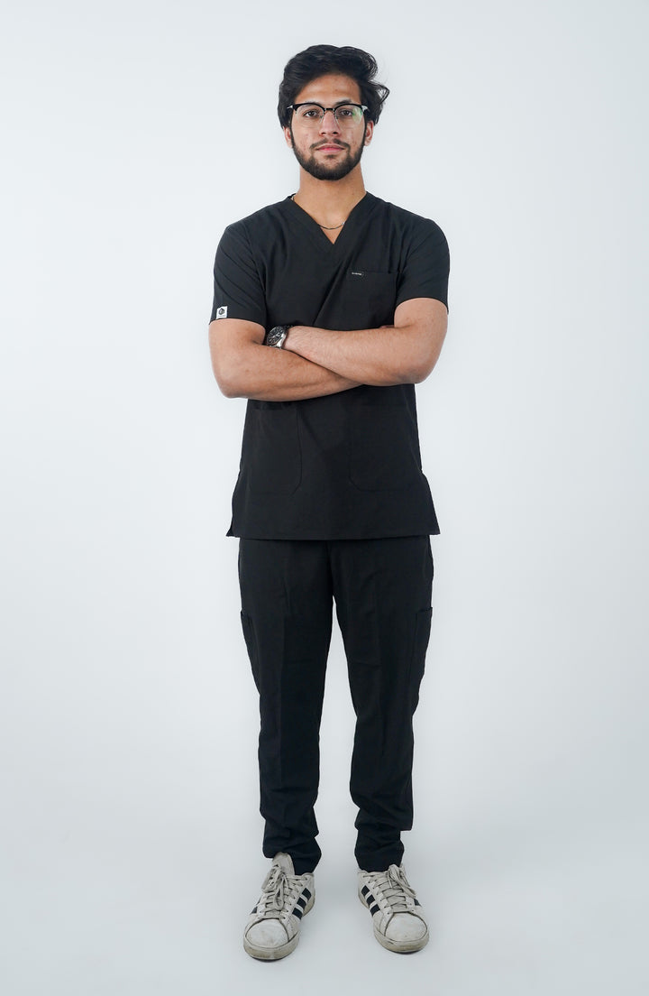 A person standing against a white background, wearing a black short-sleeved shirt and pants, with a pair of glasses and white sneakers.