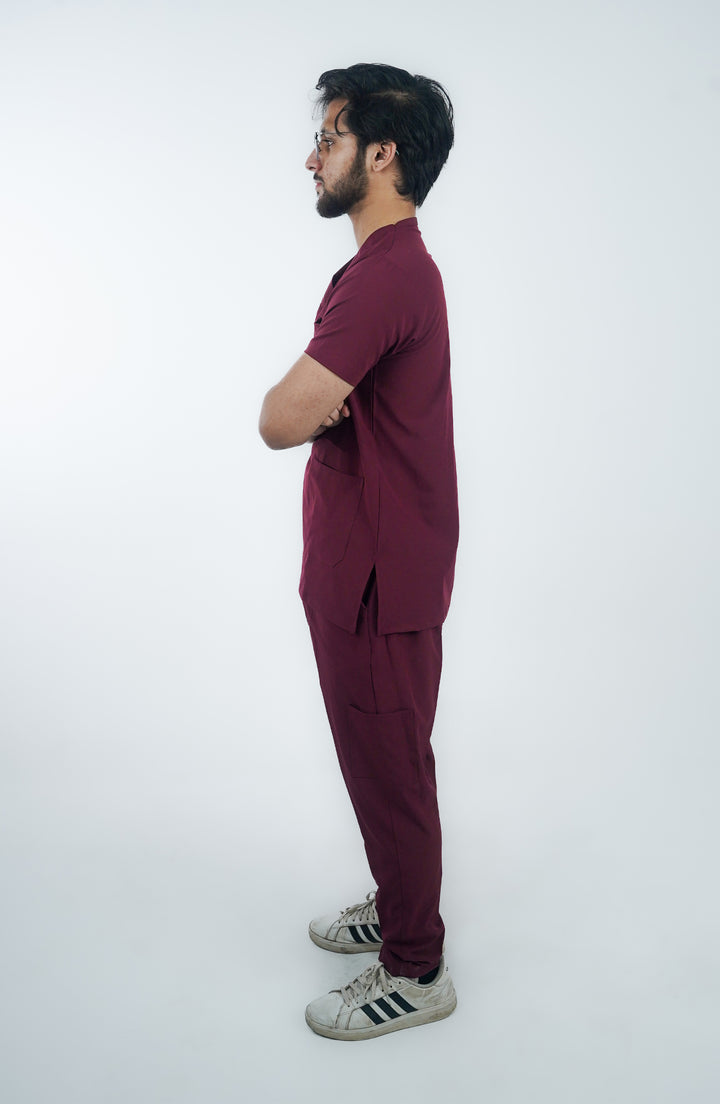 Side profile of a male healthcare worker in elegant maroon scrubs, hands in pockets.