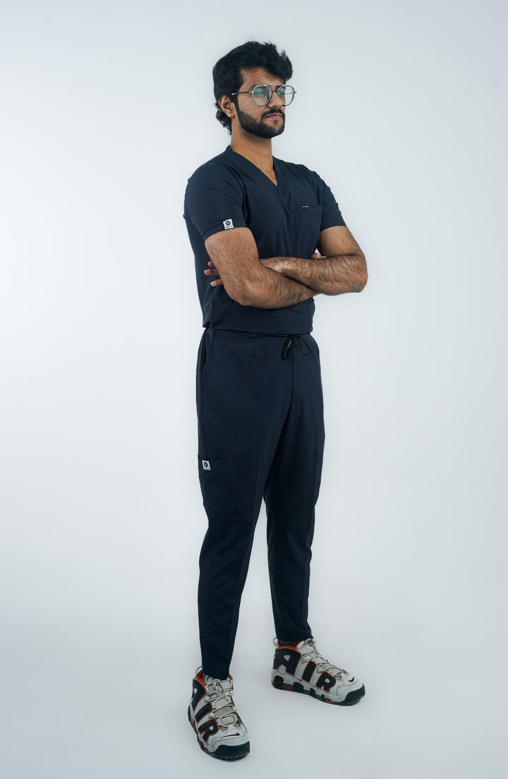 A person standing against a white background, wearing navy scrubs and white sneakers.