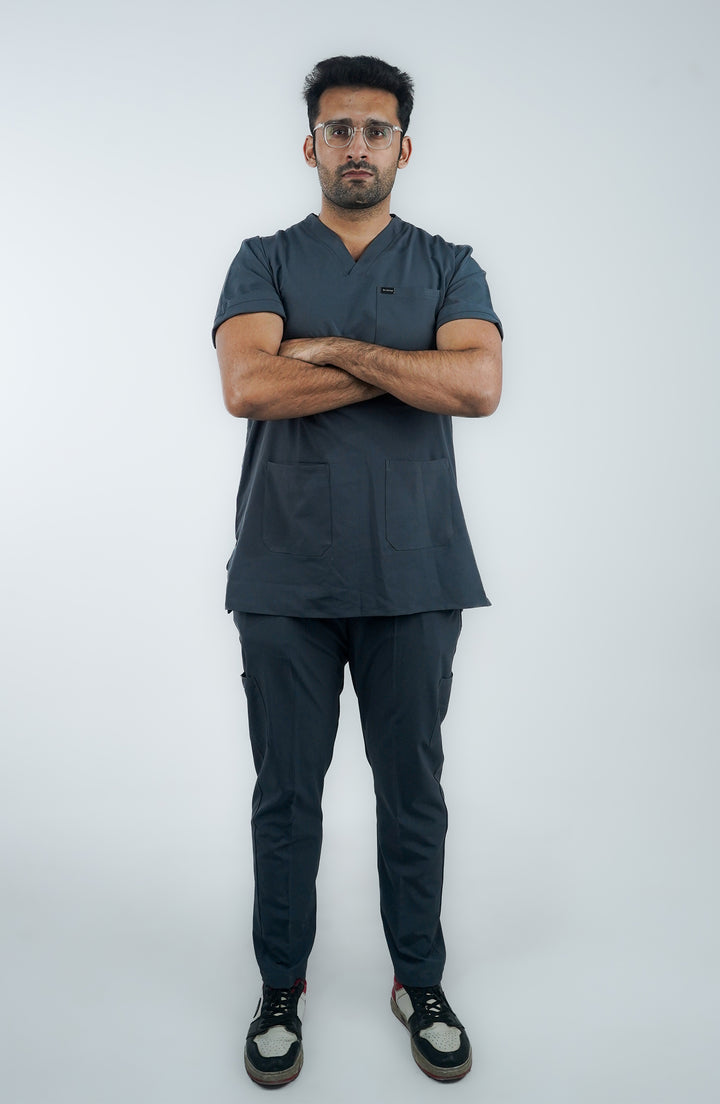 A person standing with their arms crossed wearing a slate gray medical uniform, consisting of pants and a shirt with short sleeves.